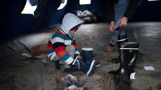 Young Syrian boy puts on a pair of boots