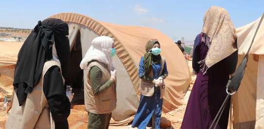 Three masked members of one of the Volunteer First Response Committees conduct awareness-raising in an IDP camp