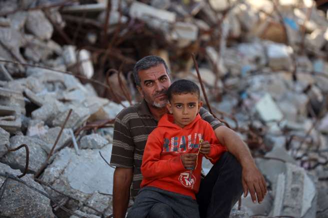 Man sits with son amidst rubble