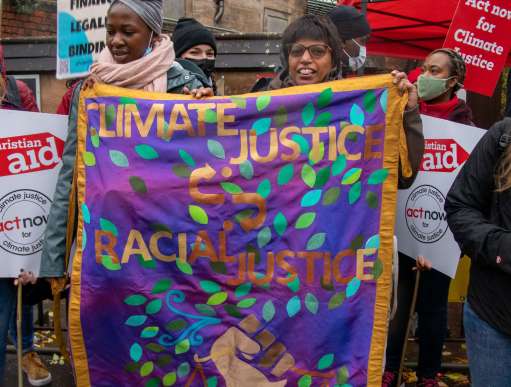Radhika Bynon holds a purple banner reading Climate Justice Racial Justice