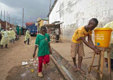 Boy in street in Sierra Leone washing his hands at wash station set up to control Ebola.