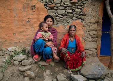 A grandmother, mother and child sit outside their collapsed home in India
